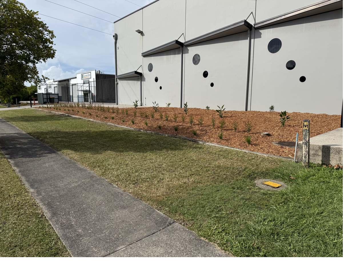 Newly installed and mulched garden bed edged flush to the footpath at a Warana industrial property