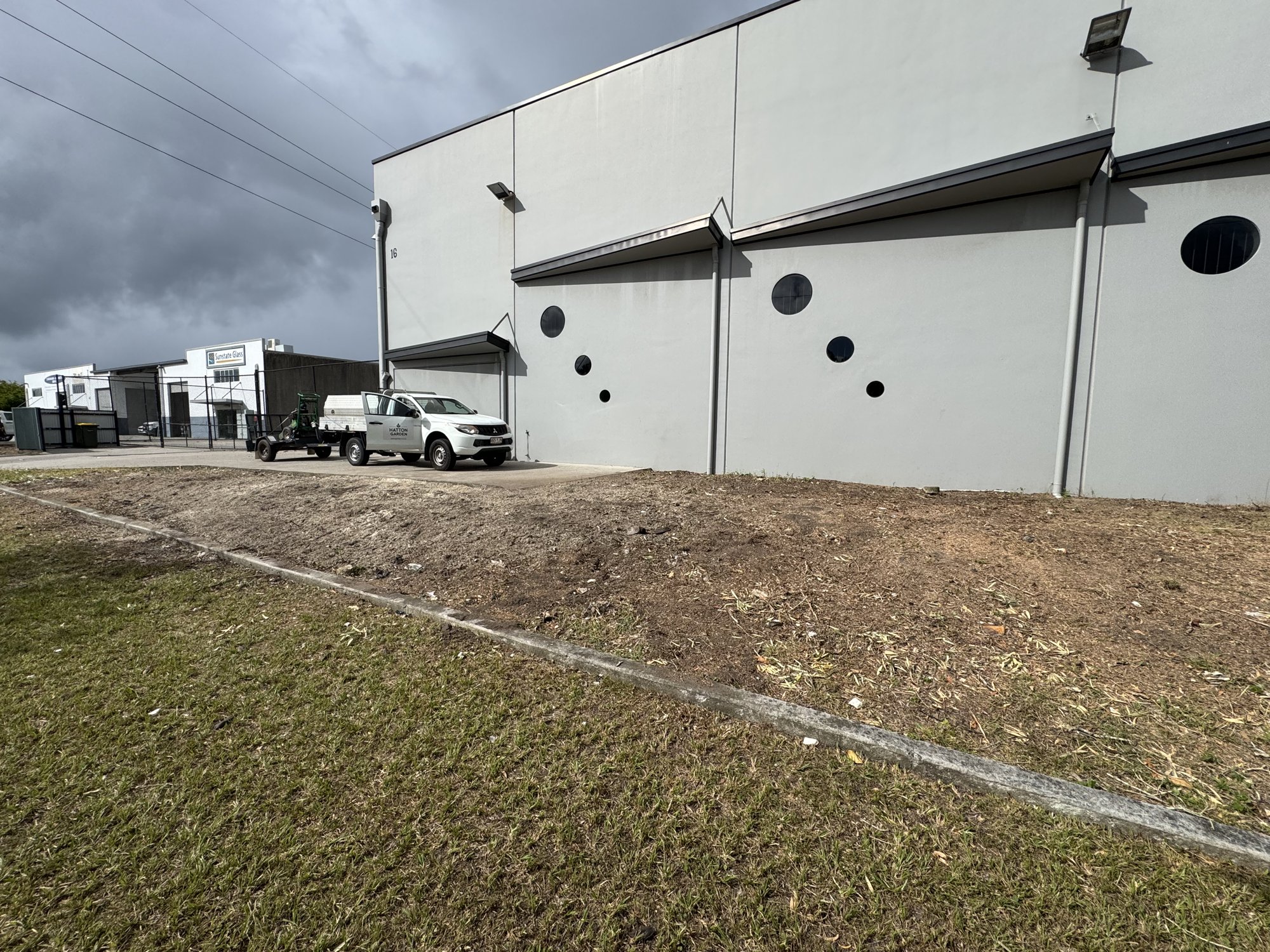 Bare, patchy bank along an industrial unit wall before the garden bed was installed